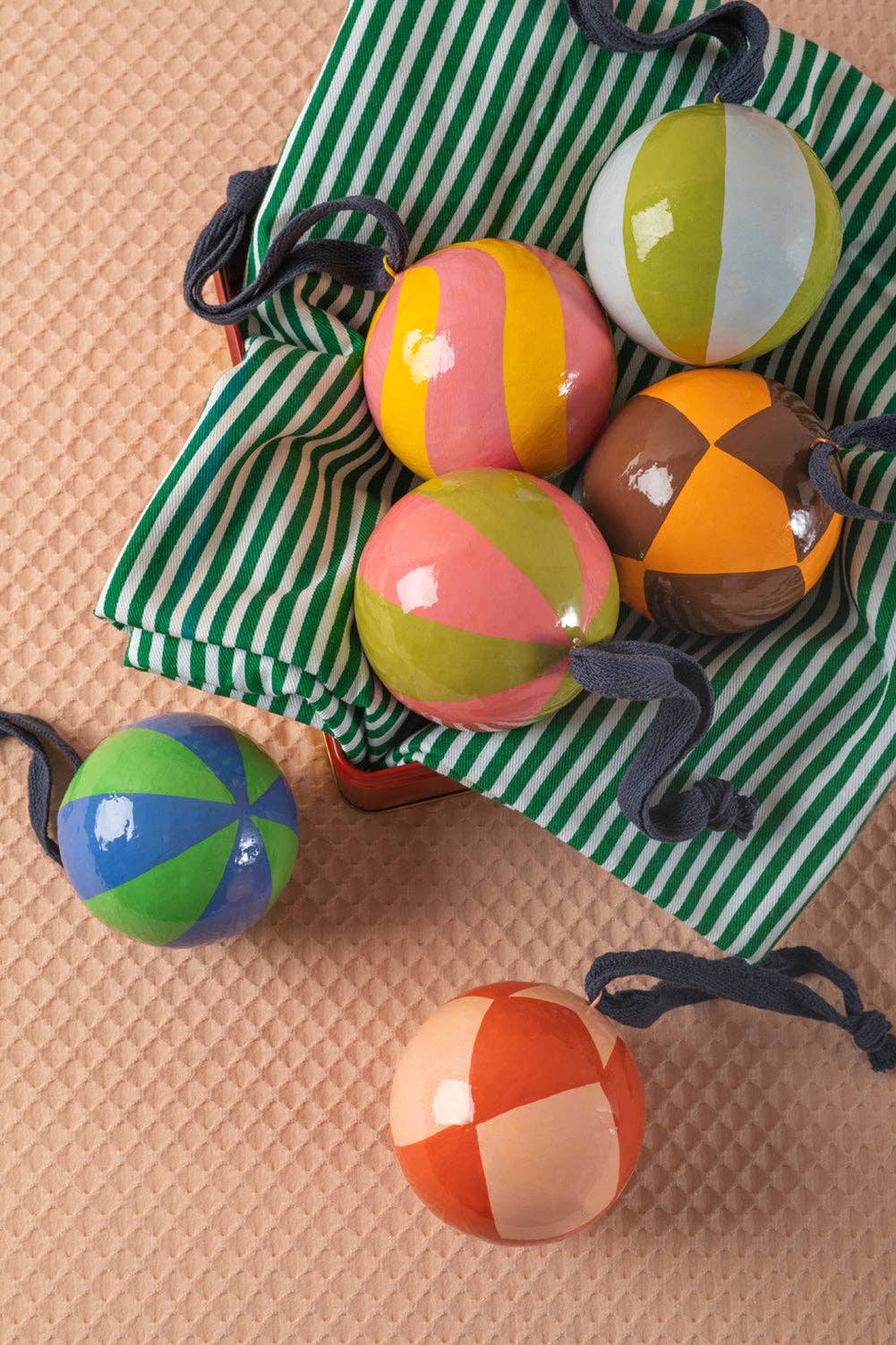 Colorful striped balls on a green and white striped bag on a beige surface